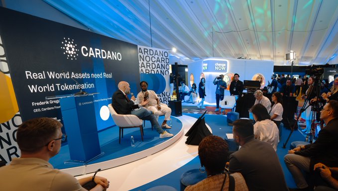 A panel discussion titled 'Real World Assets need Real World Tokenisation' featuring Frederik Gregaard, CEO of Cardano Foundation, takes place at a Cardano booth during a crypto conference.