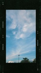 A photograph of a bright sky with wispy clouds and a street lamp at the bottom, viewed through a dark vertical frame or doorway.