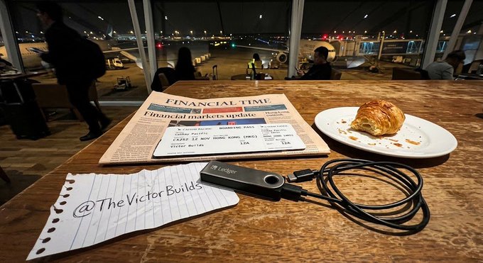 A croissant, laptop, and a Financial Times newspaper with a handwritten note "@TheVictorBuilds" sit on an airport lounge table as night flights prepare outside, visually capturing the distracted retail sentiment while major geopolitical news unfolds between Washington and Beijing.