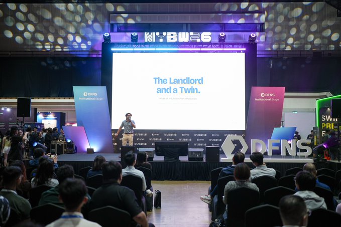 A conference photograph from MYBW 2026 showing a speaker on stage at the DFNS Institutional Stage presenting "The Landlord and a Twin," with a large audience seated in the foreground.