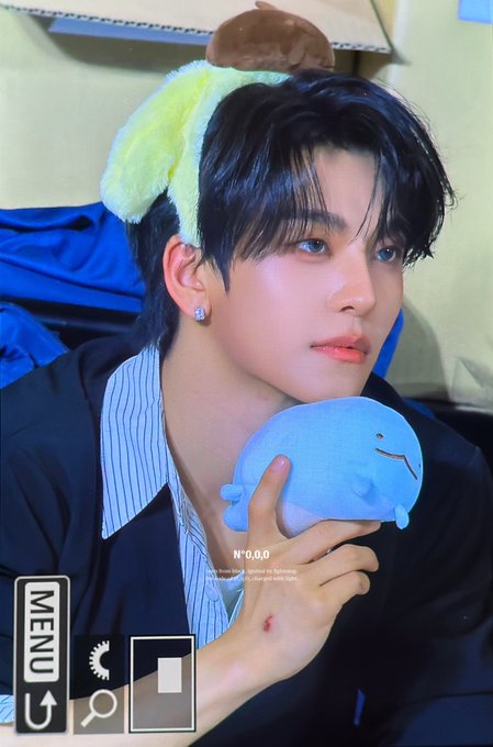 A young man with dark hair wearing a yellow fuzzy headband and holding a blue whale plushie appears on what looks like a camcorder viewfinder screen displaying "N°0.0.0," "MENU," and timestamp elements, fitting the playful, quirky aesthetic of the post tagged with #허씬롱 #XINLONG #贺鑫隆 #ALPHADRIVEONE #ALD1.