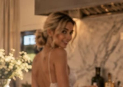 A blurry, intimate photo of a smiling blonde woman turning her head toward the camera in a softly lit, marble-walled kitchen setting.