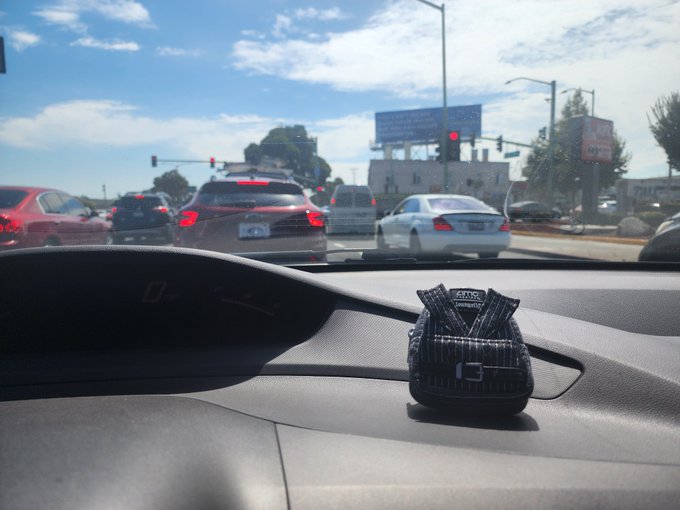 A photo taken from inside a car at a traffic light, showing a small decorative patterned handbag sitting on the dashboard with other vehicles and a road ahead.