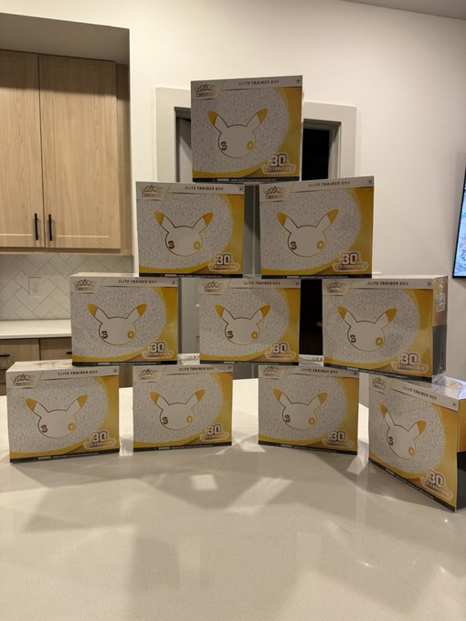A stack of ten Pokemon Elite Trainer Box packages featuring Jolteon, arranged on a kitchen counter.