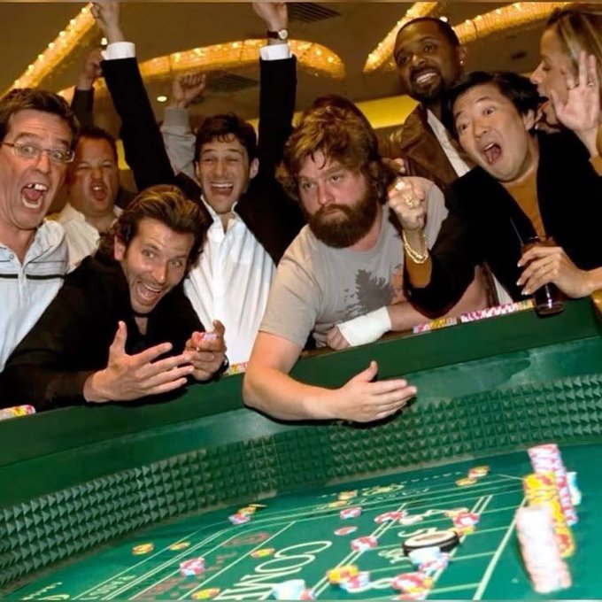 A group of excited men cheering at a green felt craps table in a casino, with chips scattered across the betting surface.