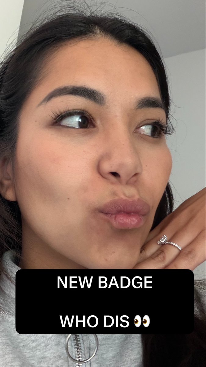 A selfie of a young woman looking to the side with her hand resting on her chin, with text overlay reading 'NEW BADGE WHO DIS 👀'.