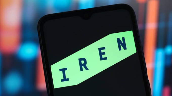 A close-up of a smartphone displaying the green IREN logo against a dark screen, set against a blurred background of colorful financial charts.