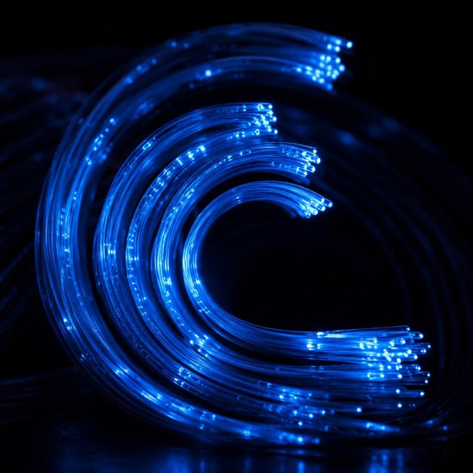 Close-up photograph of glowing blue fiber optic cables spiraling in a circular pattern against a black background.