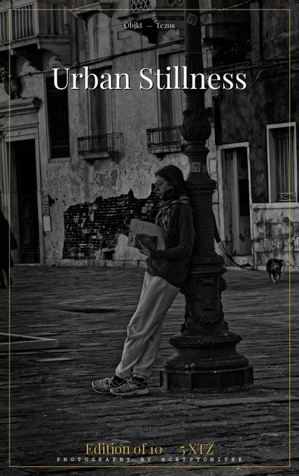 A black and white NFT photography print titled "Urban Stillness" by @cryptonitek, showing a person reading a book while leaning against a lamppost in a cobblestone street.