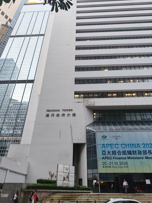 The Wanchai Tower in Hong Kong displays an APEC China 2026 Finance Ministers' Meeting banner scheduled for 20-21.10.2026, providing a fitting backdrop for CZ's announcement of his arrival in the city. The post suggests he's likely in Hong Kong for the major finance summit, where he may have meetings or events planned.
