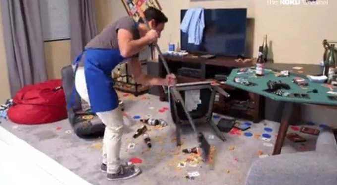 A man in a blue apron and gray shirt appears to be smashing a chair in a messy living room, captured from what seems to be a KOKU Channel broadcast.