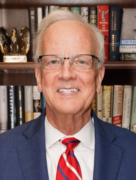 A smiling older man with glasses, wearing a navy suit and red striped tie, poses in front of a bookshelf displaying titles including "Capitalism," "Unlikely Heroes," "Poor Economics," and "The I.R.S."

The image appears to be an official portrait, though the caption identifying him as Senator Jerry Moran cannot be confirmed from the visual content alone—the bookshelves and formal headshot style suggest a professional or political setting.