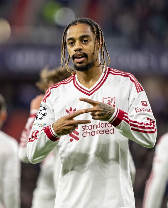 A Liverpool FC soccer player wearing a white Adidas away kit with 'Standard Chartered' sponsorship makes a hand gesture during a Champions League match.