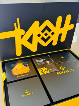 A Binance promotional box set with the Binance logo in yellow, containing various branded merchandise items including cards and stickers.