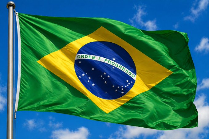 The Brazilian flag waves against a blue sky, displaying its iconic green and yellow design with a blue globe bearing the national motto "ORDEM E PROGRESSO." The image accompanies news that Brazil has taken the strictest regulatory action against prediction market platforms, banning services like Polymarket and Kalshi by blocking them at the telecom level.