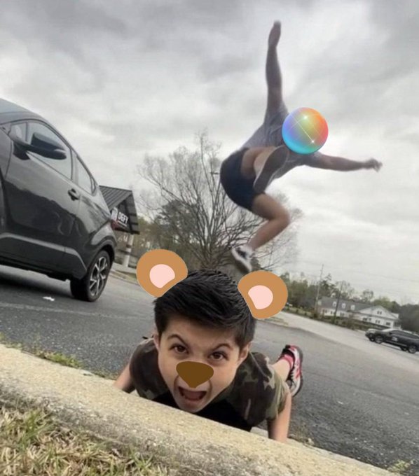 A humorous outdoor photo with a dog-ear and nose filter applied to a boy lying on the ground, while another person appears to be doing a handstand with a colorful ball filter over their head, set against a suburban street background.