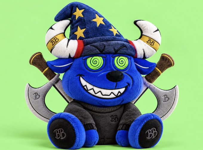 A blue plush toy character with hypnotic swirl eyes, wearing a wizard hat with gold stars and devil horns, sits against a green background with crossed axes behind it and "BB" markings on its accessories.