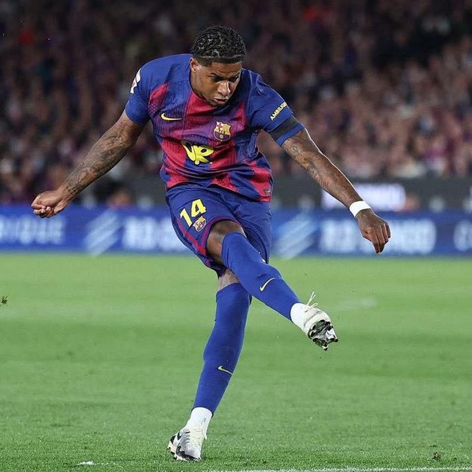 The image features a soccer player wearing blue and yellow uniform who has just kicked the ball, sending it flying across the field. The player's position near the center of the image suggests that he might have been attempting to score a goal or make an important play during the game. In the background, there are several people watching the match from various locations around the field.