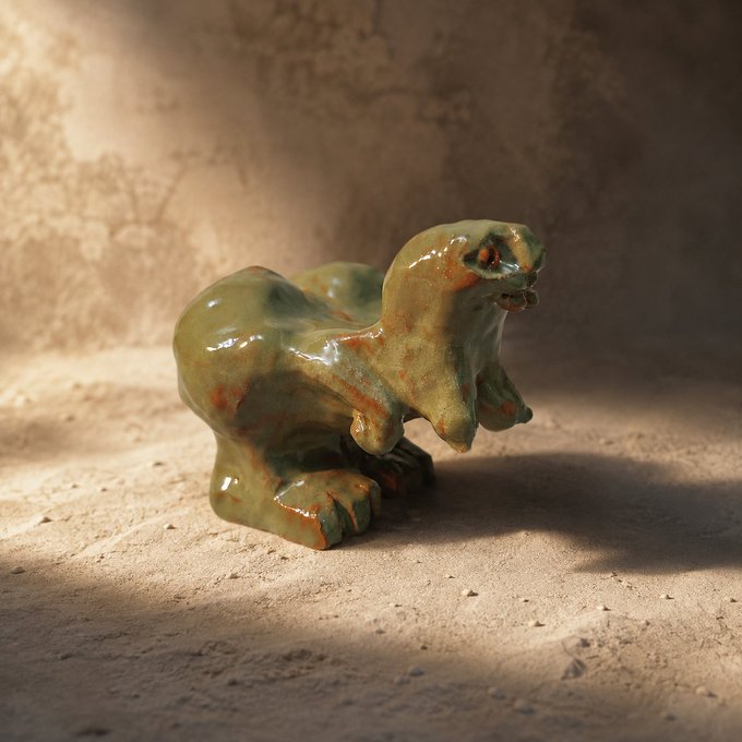 A small ceramic figurine of a green and orange creature sits on a textured surface, illuminated by warm lighting that casts a long shadow to the right.