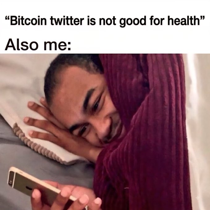 A meme captioned "'Bitcoin twitter is not good for health' Also me:" featuring a smiling person wrapped in a maroon blanket looking at a smartphone in bed.