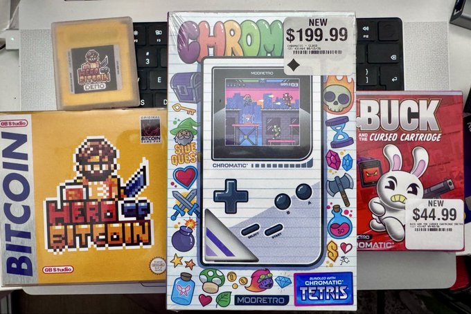 Three retro gaming items for sale: 'Hero of Bitcoin' by BITCOIN (new $199.99), a Modretro 'CHROMATIC' handheld console bundled with Tetris, and 'Buck and the Cursed Cartridge' (new $44.99).