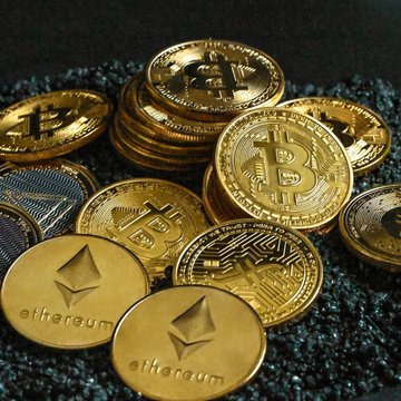 A pile of gold Bitcoin and Ethereum cryptocurrency coins rests on a dark surface, featuring visible "ethereum" text and the Bitcoin "B" logo. The image visually represents the digital assets and wallets referenced in the post about a global pilot program testing quantum-resistant infrastructure for secure cryptocurrency transfers.