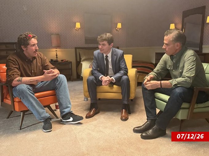 Three men sit in a circle of armchairs (orange, yellow, and green) in a warmly lit room with vintage sconces, engaged in conversation. The timestamp "07/12/26" appears in red in the bottom right corner, fitting the post's "what a time to be alive" sentiment by capturing a casual, memorable gathering.