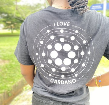 A person is shown from behind wearing a dark gray t-shirt featuring a white circular design resembling the Cardano logo with the text "I LOVE CARDANO".