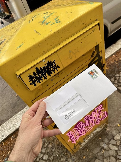 A hand holds a sealed letter in front of a weathered yellow mailbox covered in graffiti, with a postage stamp visible in the top right corner. The image illustrates the act of mailing a letter to Lukas Krieger of CDU Berlin, reinforcing the post's message about citizens writing to their representatives regarding concerns over abolishing Bitcoin's holding period.