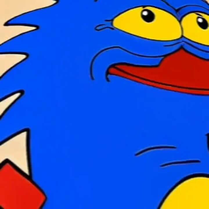 The image features a cartoon character with blue skin, red eyes, and yellow teeth. The character appears to be smiling or frowning, depending on the viewer's perspective. The character is wearing a red shirt, which contrasts with its blue body. The background of the image is white, making the colorful character stand out even more.