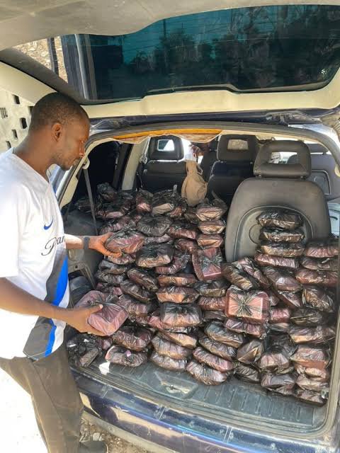 A man inspecting a large quantity of black plastic bags filled with packages loaded into the back of an SUV.