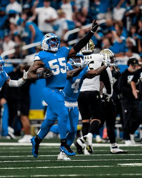 An NFL action photograph showing Detroit Lions player #55 in a blue uniform celebrating on the field during a game against the New Orleans Saints.