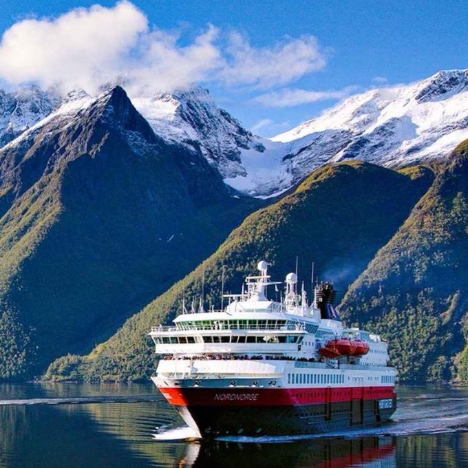 A red and white cruise ship named "NORDNORGE" sails through calm fjord waters surrounded by snow-capped mountains and lush green hillsides. The image ties to the post by showcasing a real-world maritime vessel that would be tracked by Ethra's SeaVerity system, which combines AIS data, visual evidence, and local observations to verify and score maritime information for trustworthiness.
