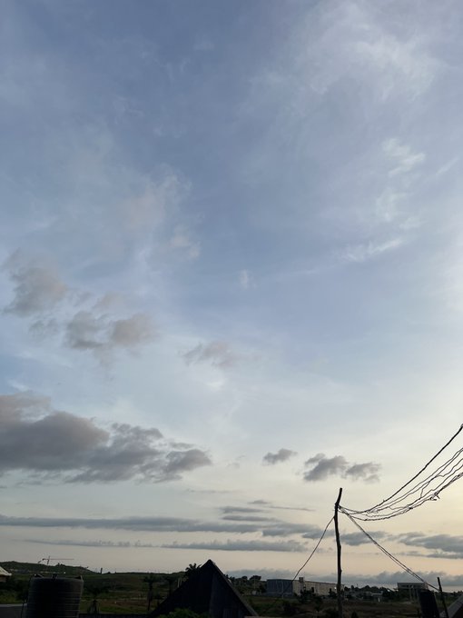 A landscape view showing a vast sky with wispy cirrus clouds over a rural area with power lines and rooftops visible at the bottom.