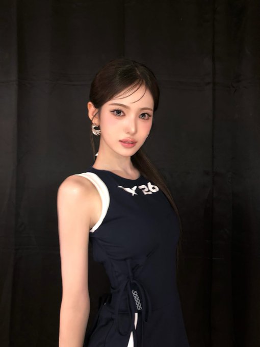 A young woman with long dark hair wearing a navy blue dress with white trim poses against a black backdrop.