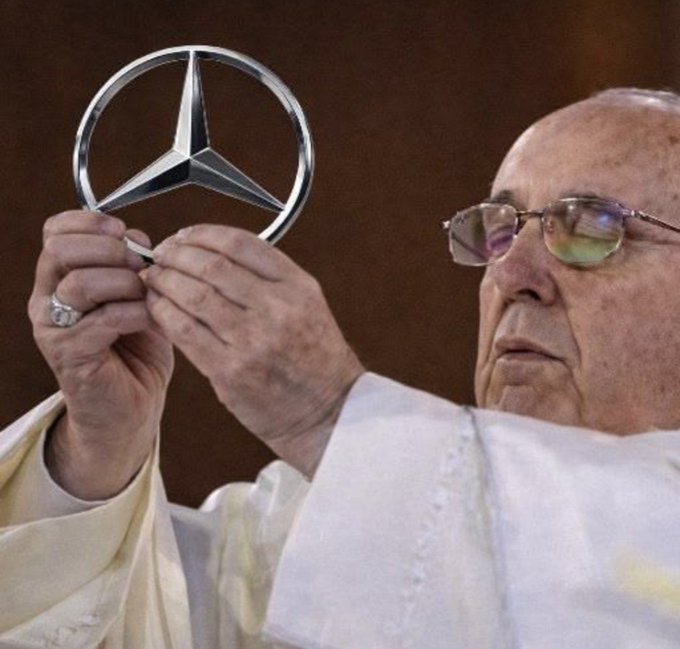 An elderly man in traditional robes and glasses holds up the Mercedes-Benz three-pointed star emblem, symbolizing the luxury "benz" lifestyle referenced in the caption, while the Mercedes logo ties directly into the "benz we drive" portion of the message. The image's focus on the iconic brand emblem visually reinforces the contrast between crypto wealth and luxury car ownership.