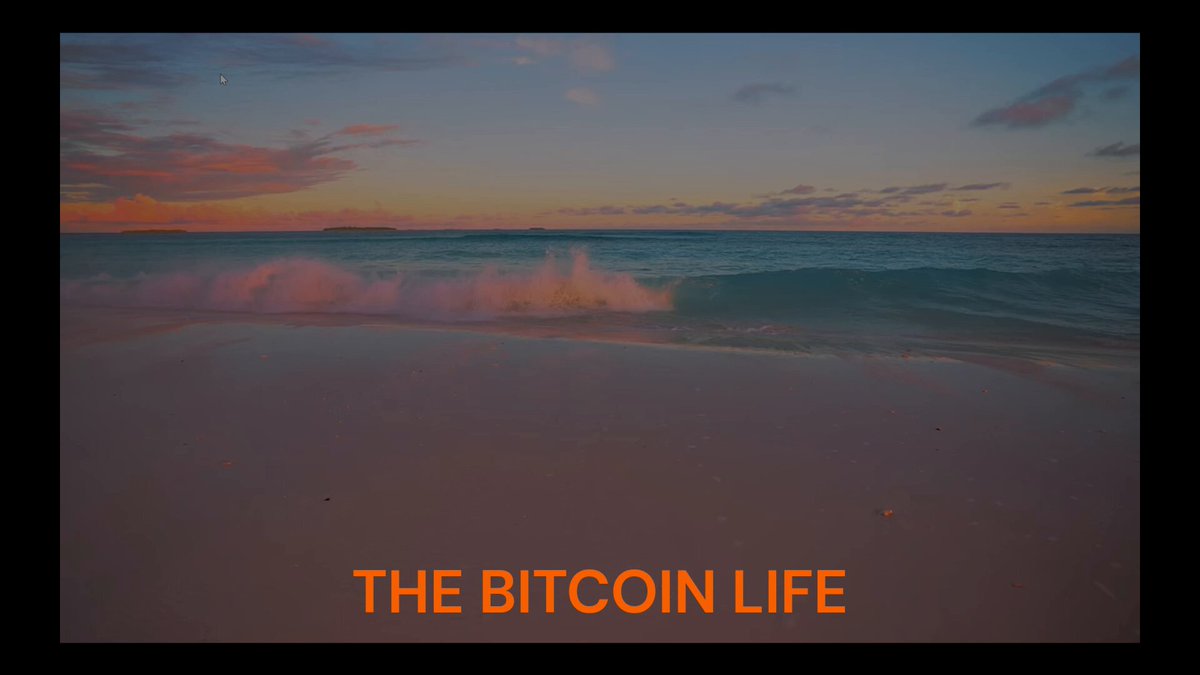 The image shows an ocean scene at sunset, with a beach setting featuring waves crashing onto the shore. The sky above has a beautiful blend of pink and orange hues, creating a serene atmosphere. In the foreground, there's text that reads "The Bitcoin Life" in bold black letters, accompanied by an orange border. This text is placed below a photo of the ocean at sunset, which adds to the overall visual appeal of the image. The combination of the beach and ocean scene with the Bitcoin life theme creates a unique and interesting juxtaposition between nature's beauty and the digital world represented by the text.