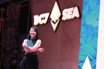 A smiling woman stands on stage pointing at the audience, with a large "DC7 SEA" sign displayed behind her, referencing the Devcon conference being promoted in the post for speaker applications to an upcoming Devcon event.