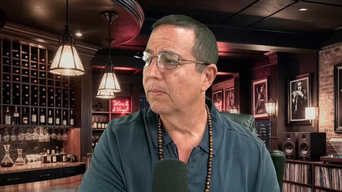 urn of wine glasses sitting on a table with a man wearing glasses and a necklace standing behind them.