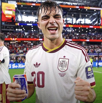 A young male soccer player wearing a white Germany national team jersey with number 20, celebrating enthusiastically on the field with a stadium crowd in the background.