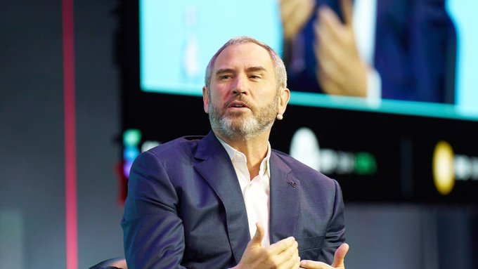The image shows a man wearing a suit, sitting down with his hands together while giving a thumbs up gesture. He appears to be at an event or conference where he is addressing an audience. The background features a large screen displaying a video of a political speech by a former US President. The caption on the image reads "INSIGHT: 
The Anti-Crypto Army was defeated...by the courts...by the voters." This suggests that the man in the suit might be discussing or advocating against cryptocurrency, possibly as part of a broader political agenda.