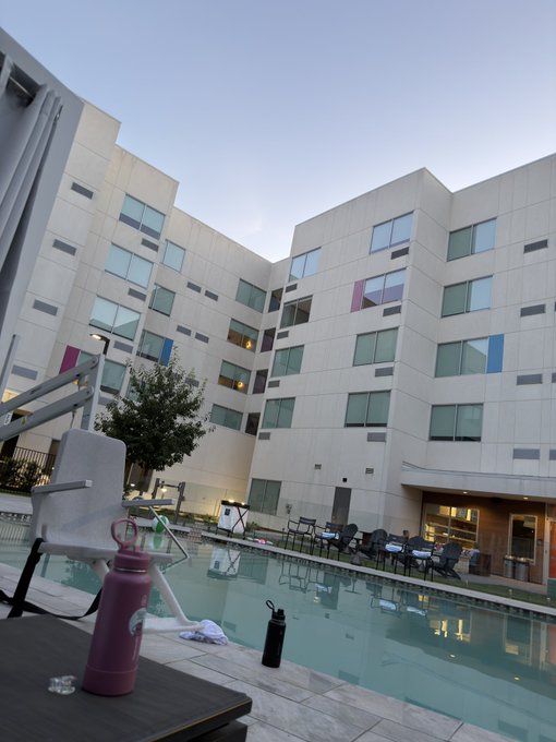 A water bottle and towel sit poolside at a hotel at sunrise, fitting a relaxed "Happy Saturday" greeting.