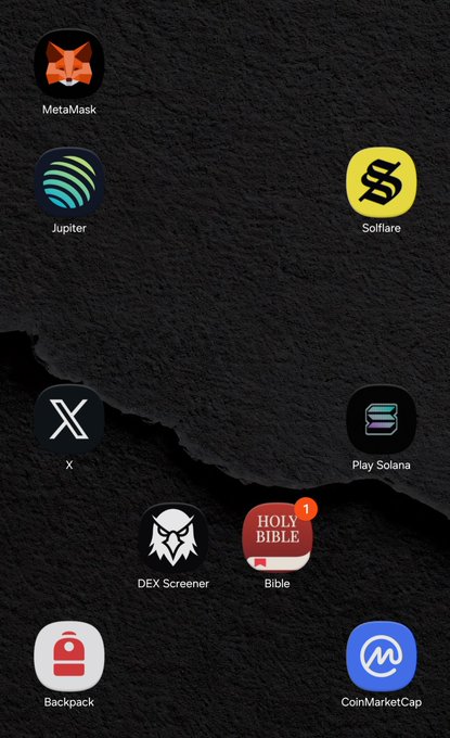 A smartphone home screen with a dark textured background displays various app icons including MetaMask, Jupiter, Solflare, X, Play Solana, DEX Screener, Bible, Backpack, and CoinMarketCap.