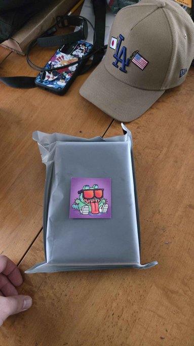 A gray padded mailer labeled with a sticker of "PSG1," the trophy from the latest @gorecats tournament, sits on a wooden floor next to a Dodgers cap and phone. The image shows the prize package received for winning first place in the tournament.