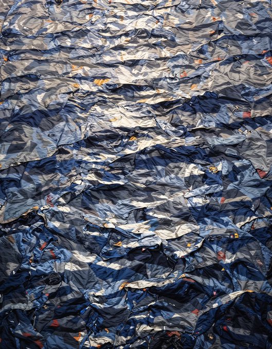 A close-up photograph of crumpled, wrinkled fabric in shades of blue, white, and gray, resembling crushed plastic or tarp material.