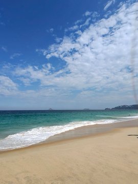 A scenic beach photograph features golden sand in the foreground, turquoise ocean waters, and a bright blue sky scattered with white clouds.
