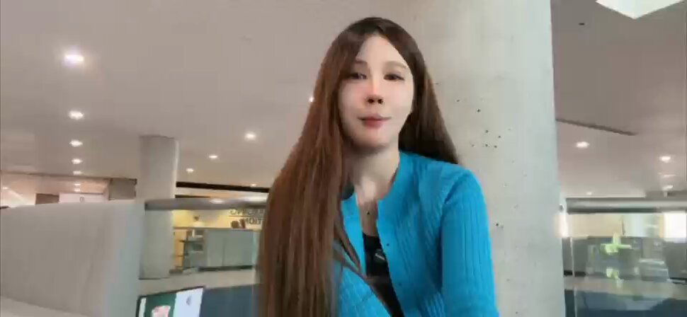 The image features a woman with long brown hair wearing a blue shirt who appears to be posing for a photo or video call. The background of the image shows an office setting with cubicles and desks, suggesting that this might be taking place at an office environment like ETH NYC.