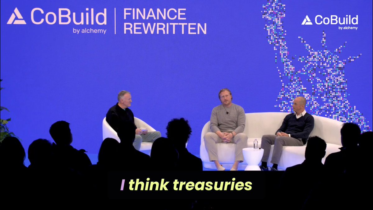 The image shows a group of people sitting around a table, with one person speaking into a microphone while others listen attentively. The scene appears to be taking place during an event or gathering where the speaker is discussing Treasuries as a potential solution for balance sheet and funding issues. The audience seems engaged in the conversation, indicating that this topic might be of interest to them.