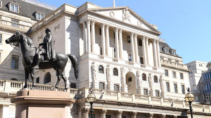 A view of the Bank of England building with its classical columns, featuring the equestrian statue of the Duke of Wellington in front and golden ornamental gates.