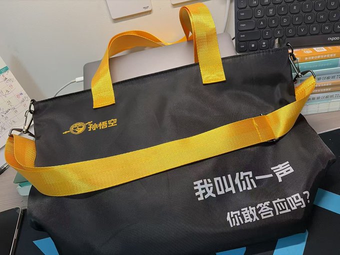 A black and yellow messenger bag with Chinese text '孙悟空' and '我叫你一声 你敢答应吗？' (referencing Sun Wukong/Monkey King), sitting on a desk near a keyboard and books.